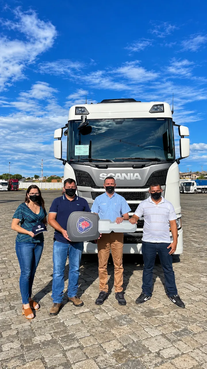 Quatro pessoas seguram a chave de um caminhão Scania branco no pátio